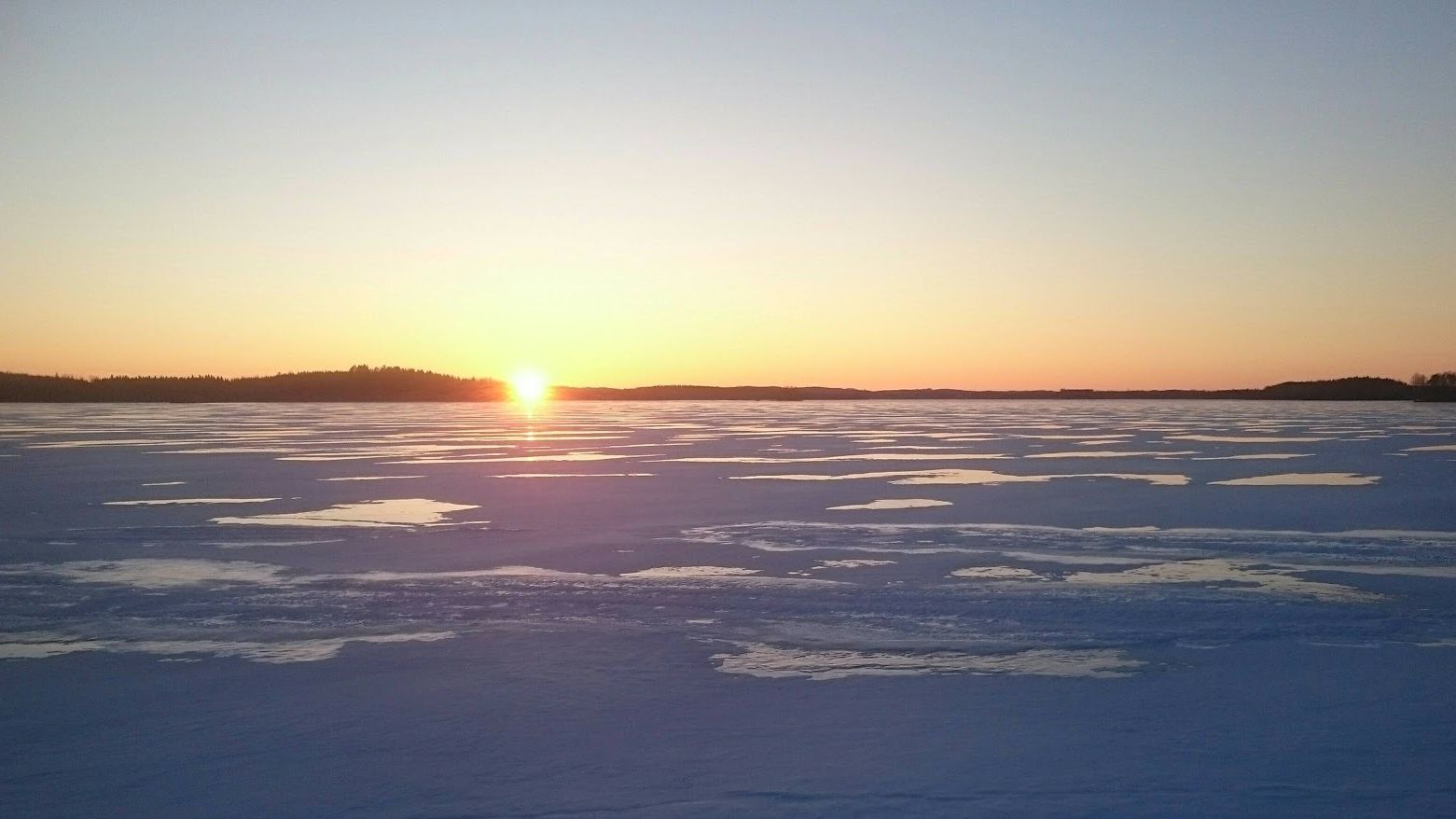 Aurinko laskee jäätyneen Simpele-järven takana.